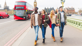 a group of students walking on a bridge in London, double decker in the background