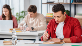A man study his book while another two students appear on the background
