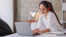 A girl listen to headphones and types on her laptop