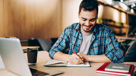 A guy writing on his notebook in front of a computer