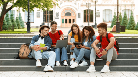 Students sit on the stairs and discuss topics they see on their tablet and laptop