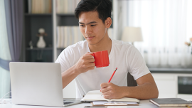 A man enjoys a cup of tea while reading his computer screen