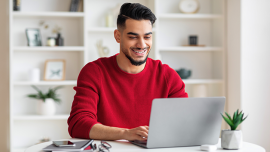 A man smiles while typing on his laptop